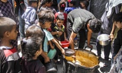Palestinian children gather around a man ladling out food from a large container
