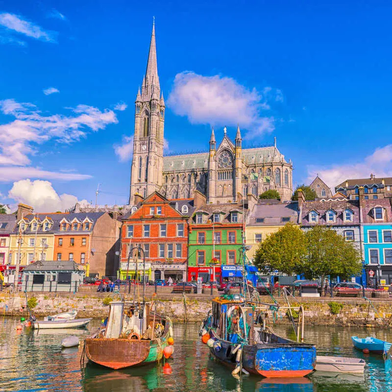The Old Port Of Cobh, In The Southern Coast Of Ireland, Lined With Colorful Houses And The Towering Cathedral Of Cobh Above Them, Ireland