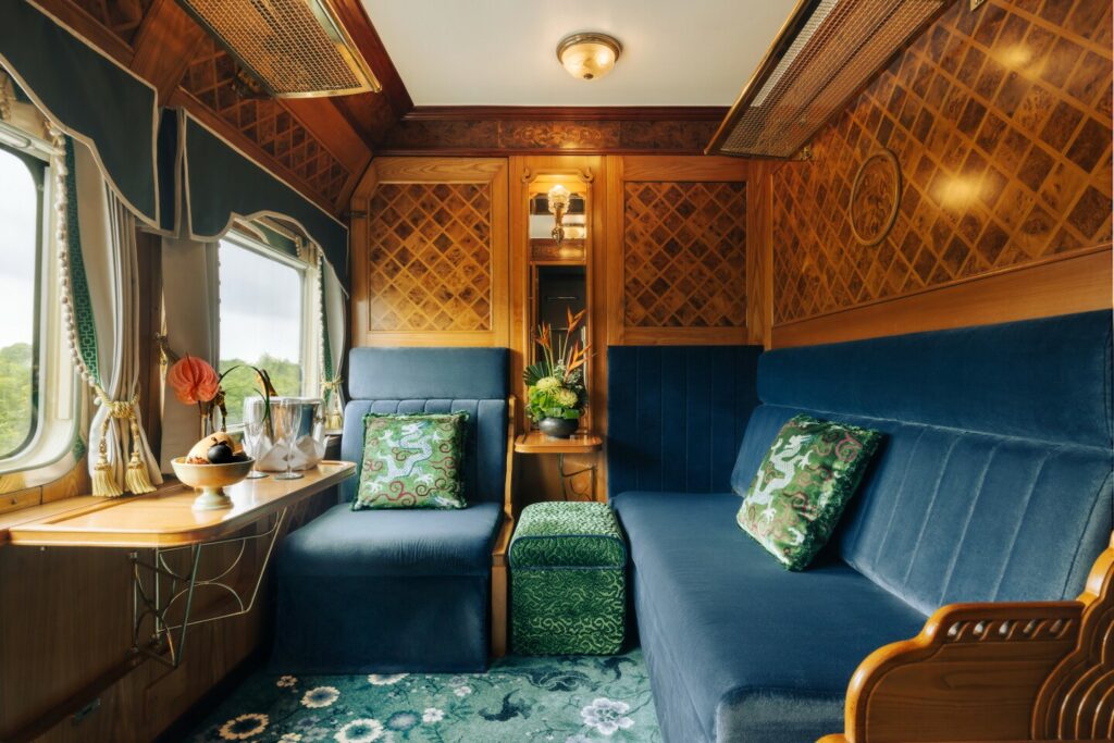 A State cabin on the Eastern and Oriental Express, with a velvet blue chair and couch and a table facing windows