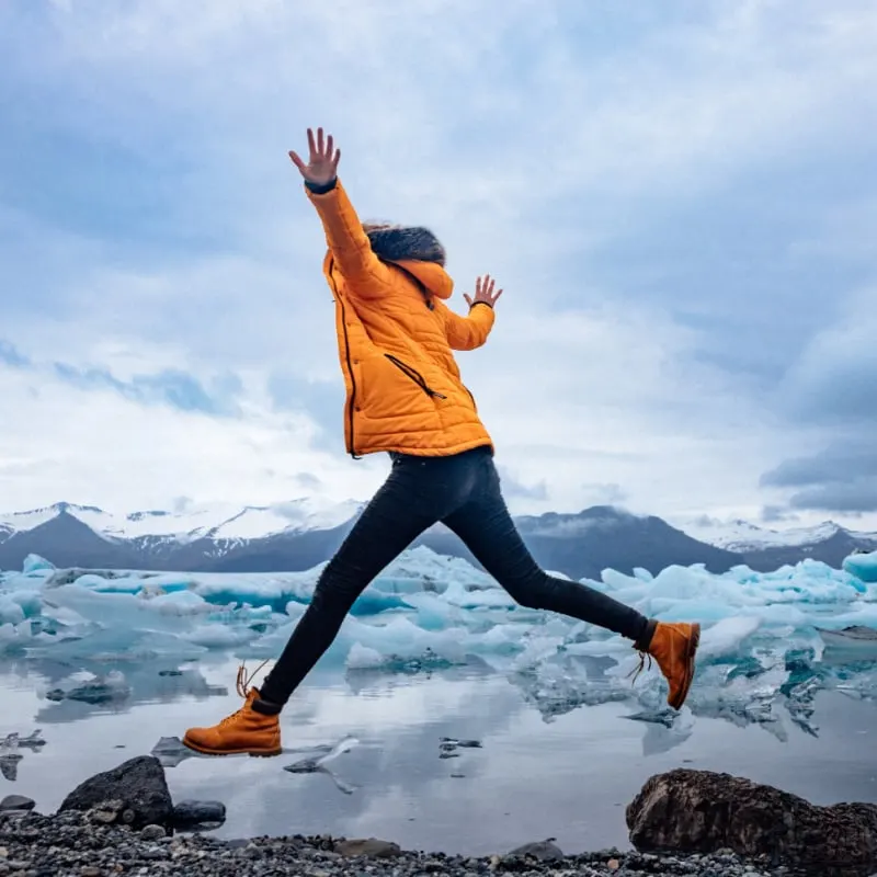 woman leaps between two rocks at Jökulsárlón lake in Iceland