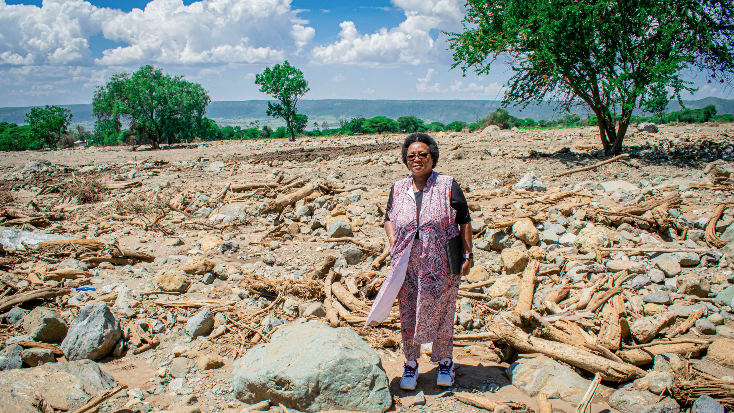 Dr. Wangeci Gatei, director of the Global Health Protection Division in CDC Tanzania, stands with the debris following flash flooding and deadly mudslides in the Manyara region of Tanzania in December 2023. Photo courtesy of Amref Health Africa in Tanzania