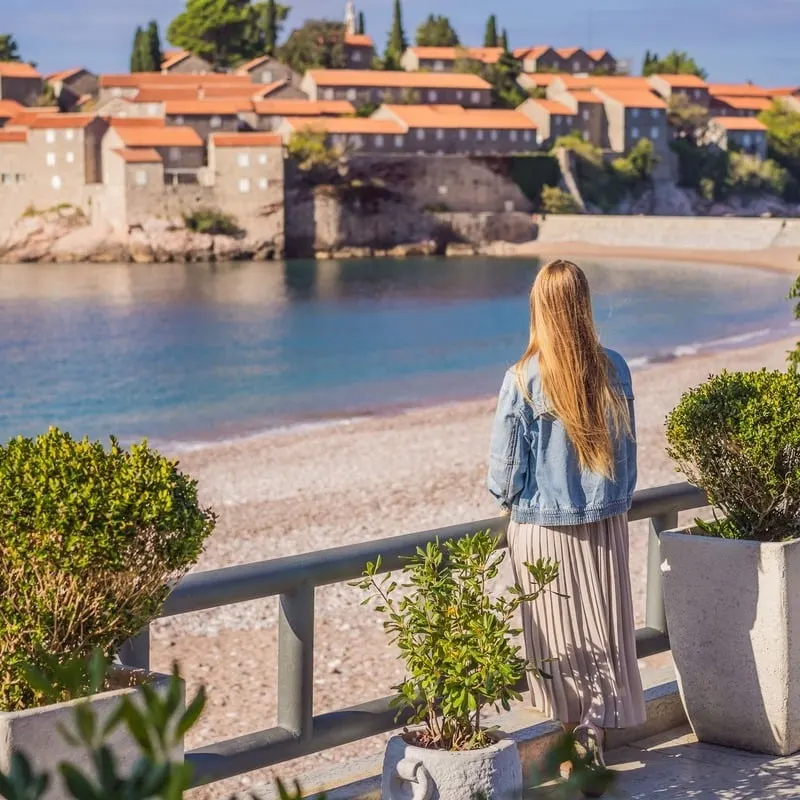 Female Tourist Observing The Sveti Stefan Resort Island In Montenegro, On The Adriatic Section Of The Mediterranean Sea, South Eastern Europe, Balkan Peninsula