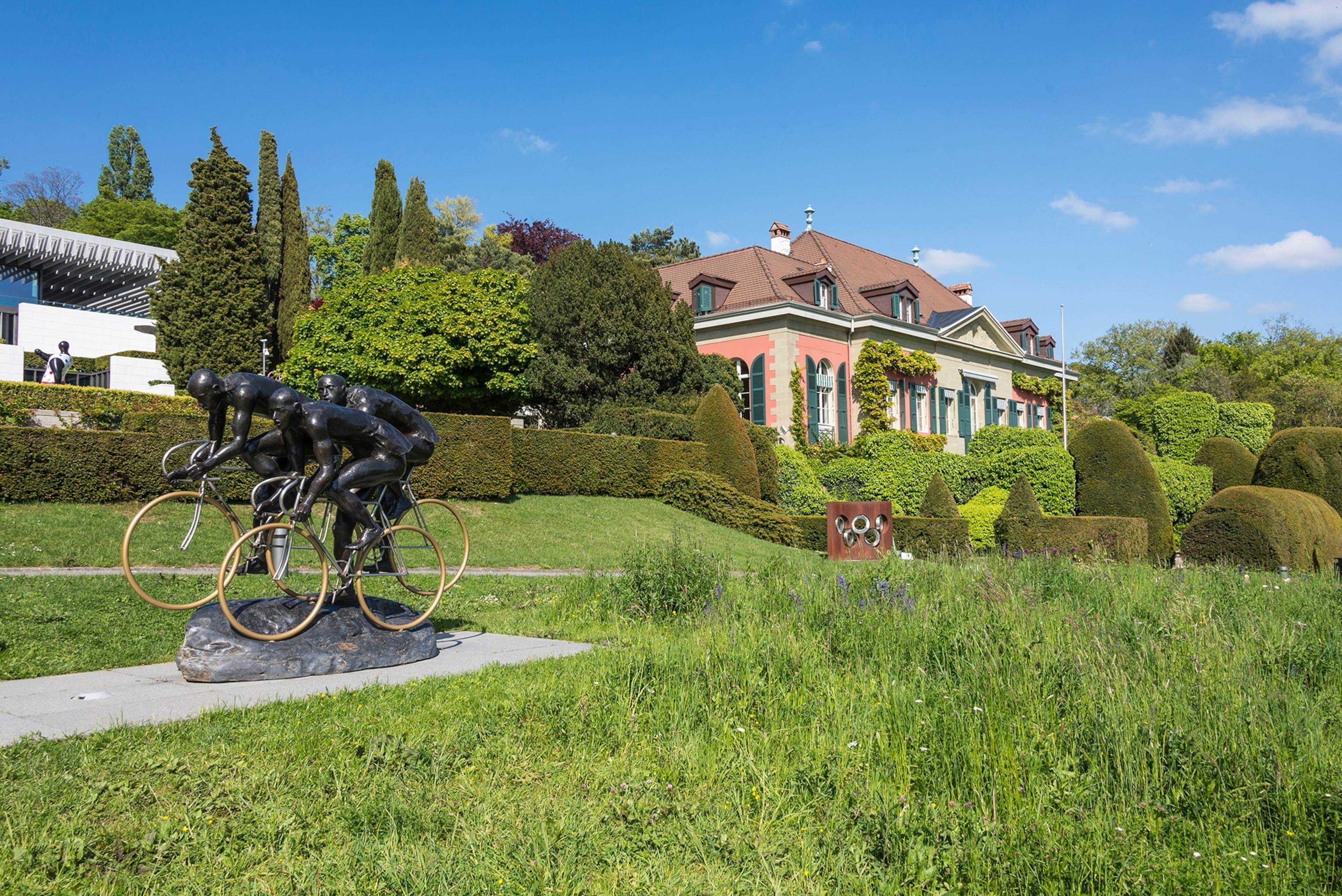 A statue of three bikers riding is surrounded by lush green landscape.