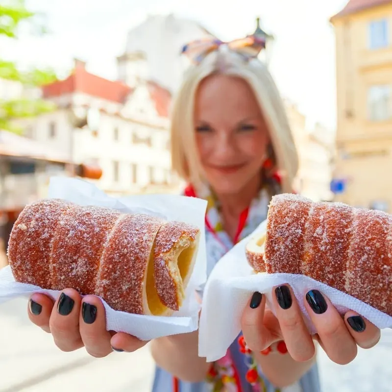 Young Female Tourist Holding Up A Pair Of Hollow Trdelníks, A Traditional Czech Dessert, In An Unspecified Old Town In Czechia, Czech Republic, Central Europe