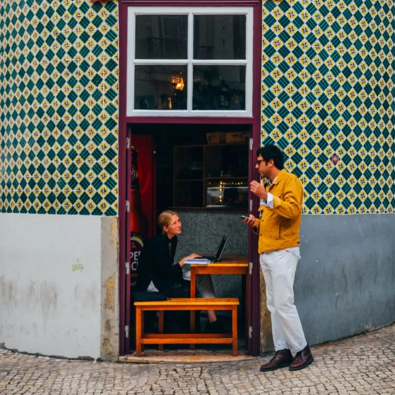 Frame of man and woman chatting at a cafe with facade of azulejo tiles in Lisbon, Portugal