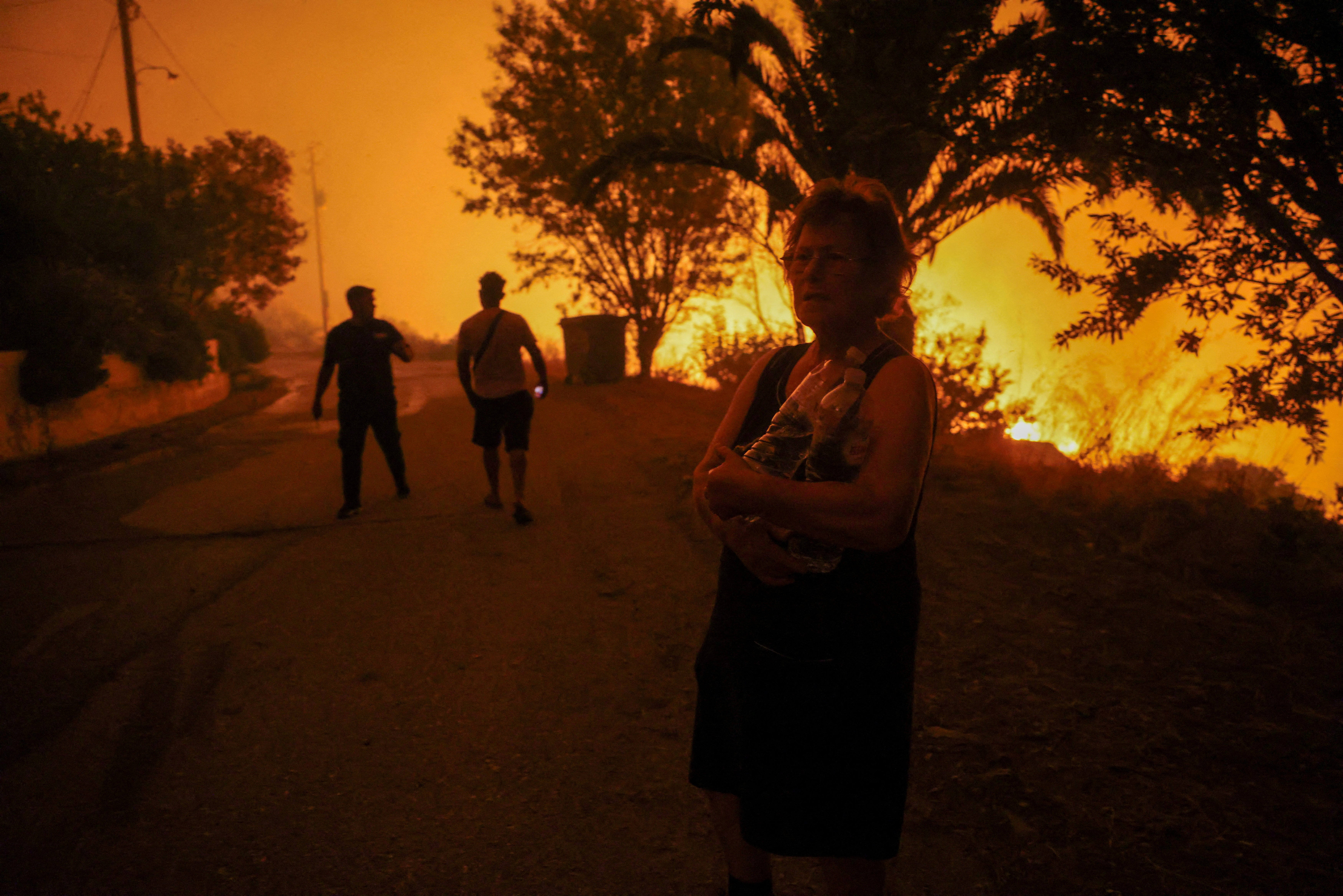 A local resident holds bottles of water next to a wildfire burning in the village of Latas, in southern Greece, on Saturday