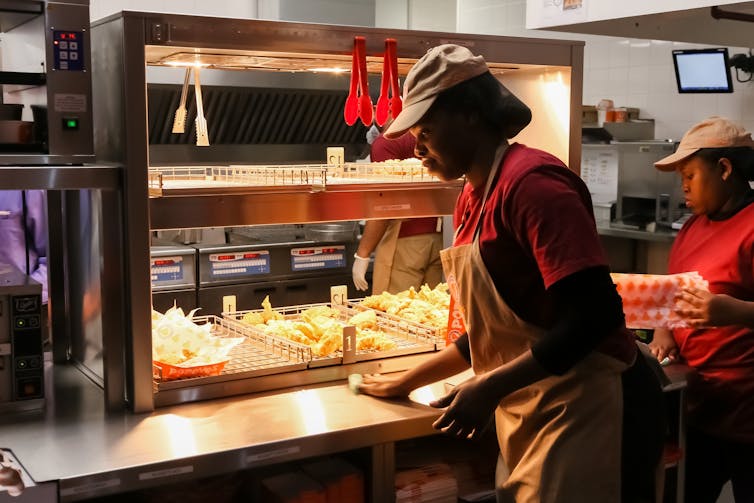 A woman in an apron and hairnet wipes down the kitchen counter at a fast food restaurant