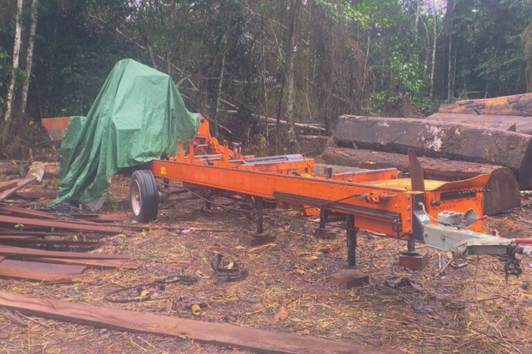 An orange-painted Woodmizer mobile mill in the forest in Liberia, a green tarp covering the engine at its rear. Image courtesy Gerald C KoinyenehTheDaylight.