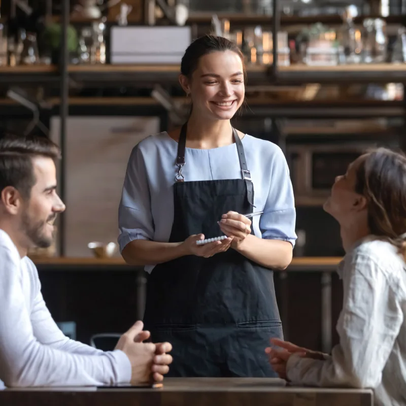 a waitress takes a food order from two people sitting at a table